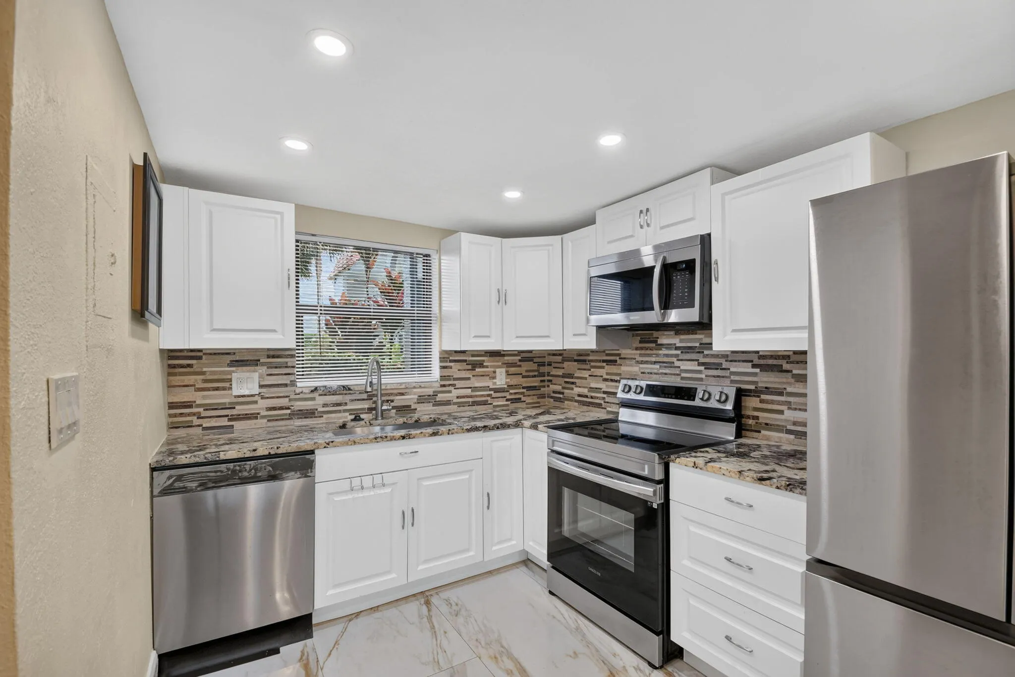 Kitchen featuring white cabinetry, stainless steel appliances, a multi-tone tile backsplash, patterned countertops, and recessed lighting