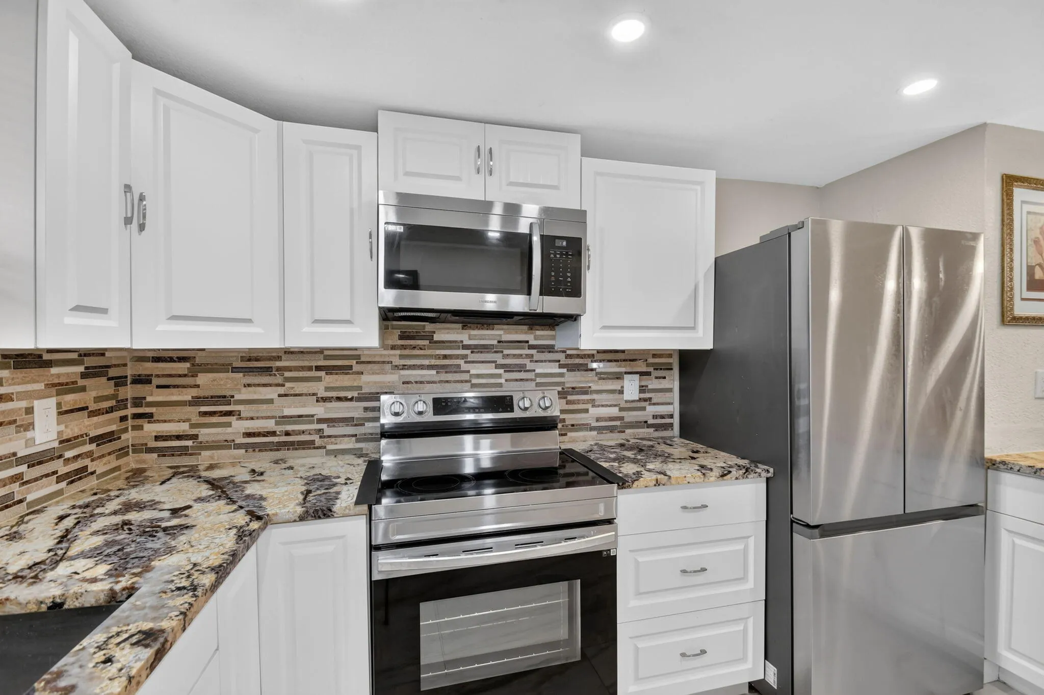 Kitchen featuring white cabinetry with brushed nickel hardware, speckled granite countertops, a linear mosaic tile backsplash, and stainless steel appliances