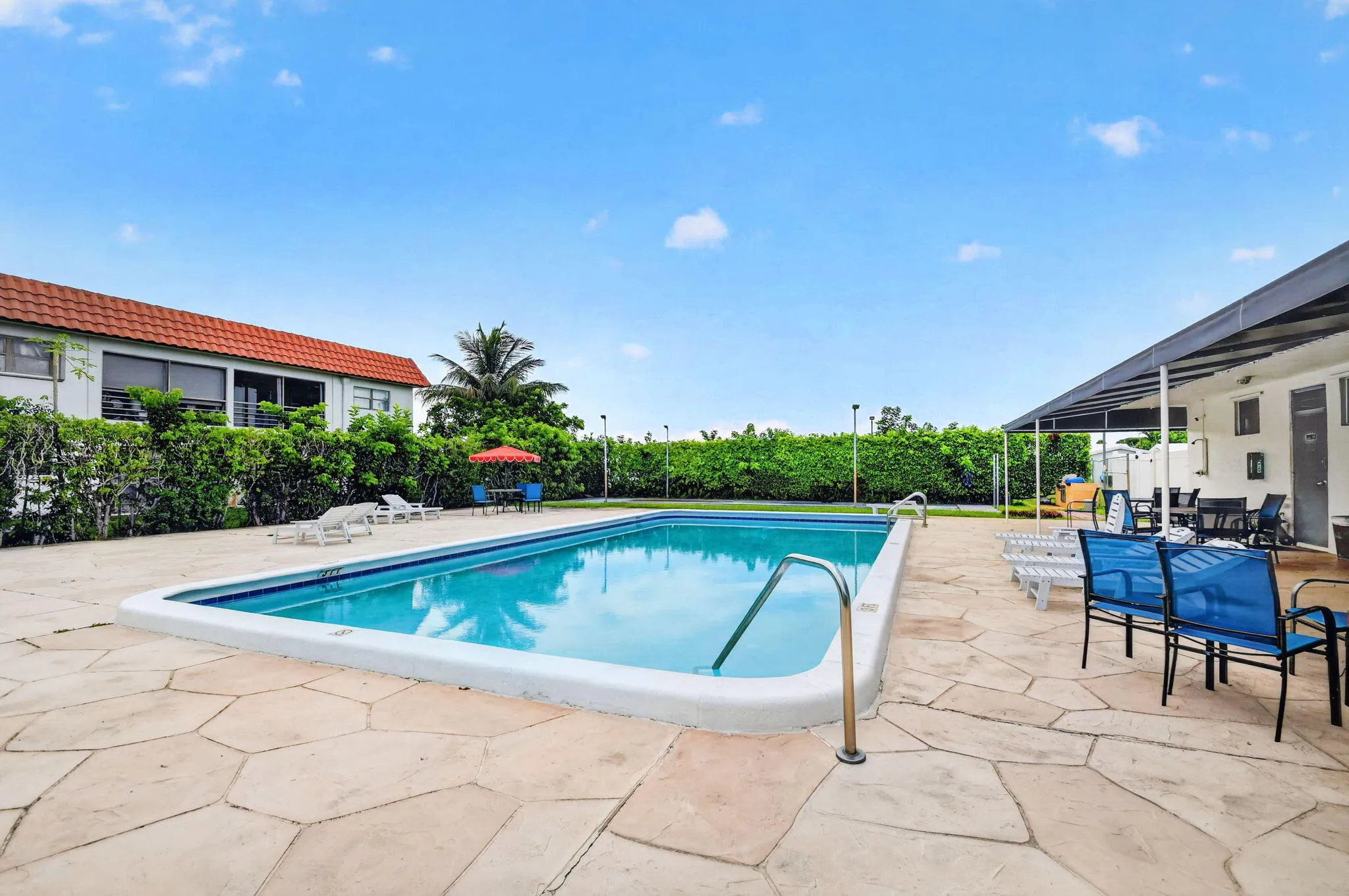 Rectangular swimming pool with integrated steps and a stainless steel handrail, surrounded by flagstone-style paving