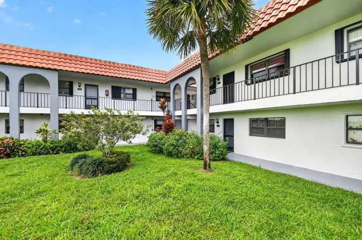 Exterior featuring a red tile roof, white stucco facade, black wrought iron railings, and a lush green lawn