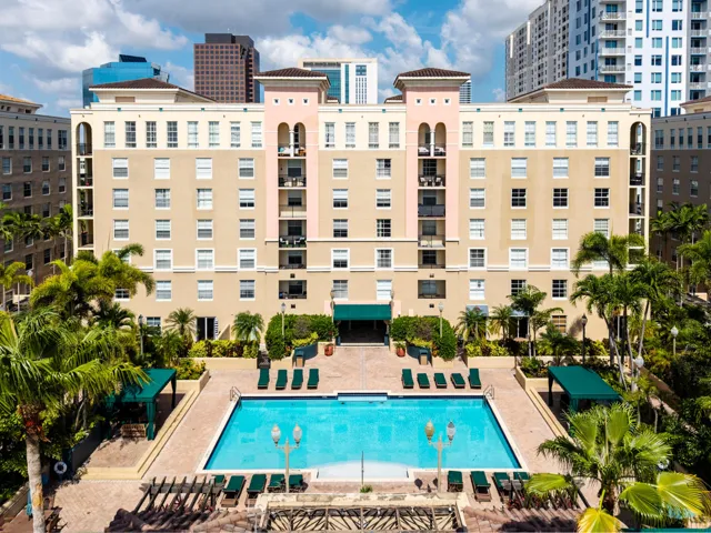 Resort-style pool deck featuring a heated pool, spa, outdoor TVs, bar, showers, and lush tropical landscaping.
