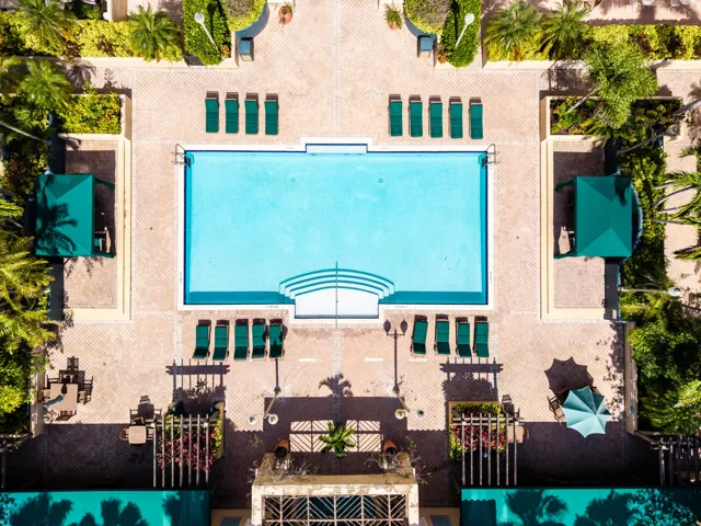 Resort-style pool deck featuring a heated pool, spa, outdoor TVs, bar, showers, and lush tropical landscaping.