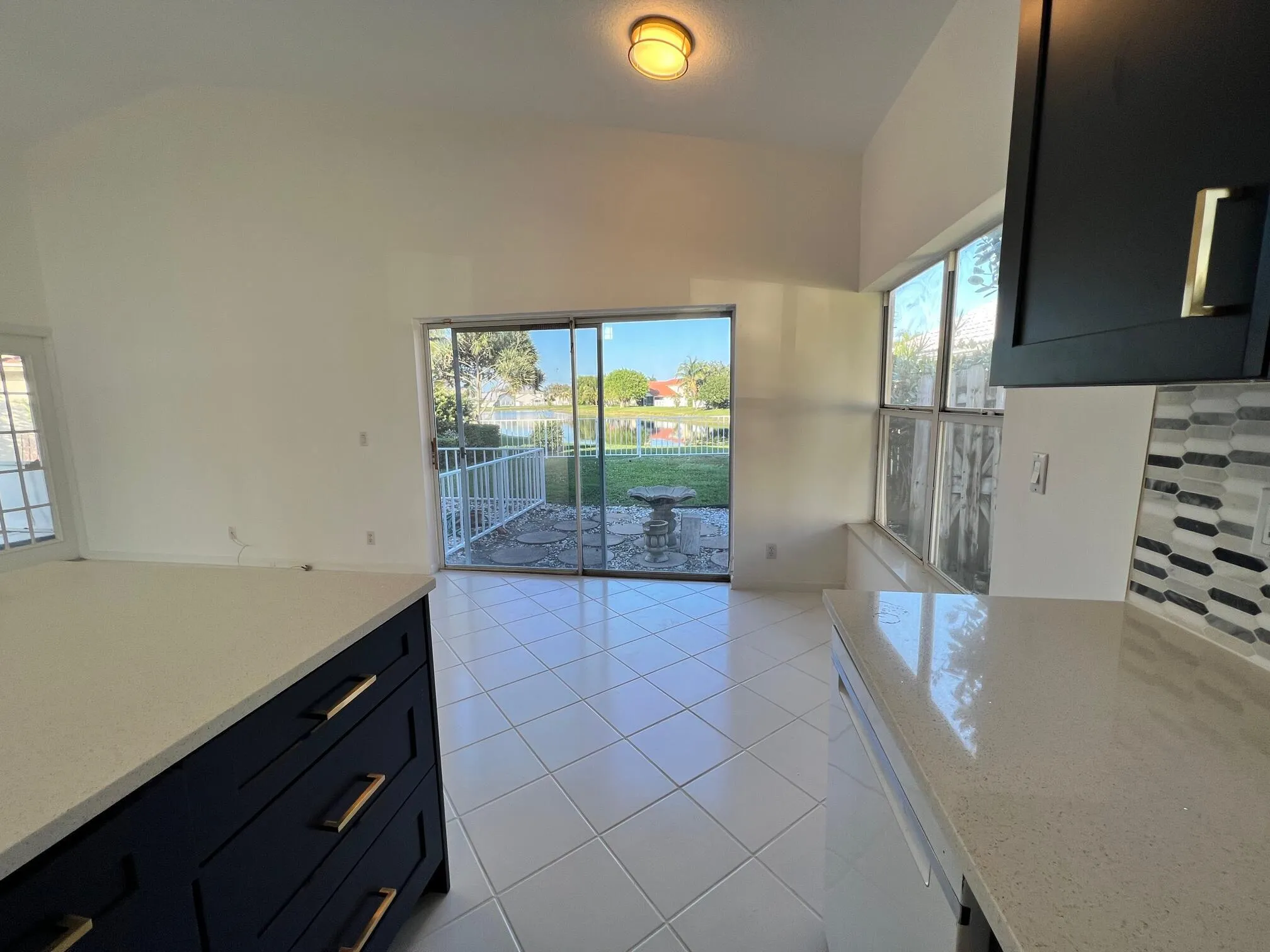 Interior space featuring white tile flooring, vaulted ceilings, and a sliding glass door leading to an outdoor patio