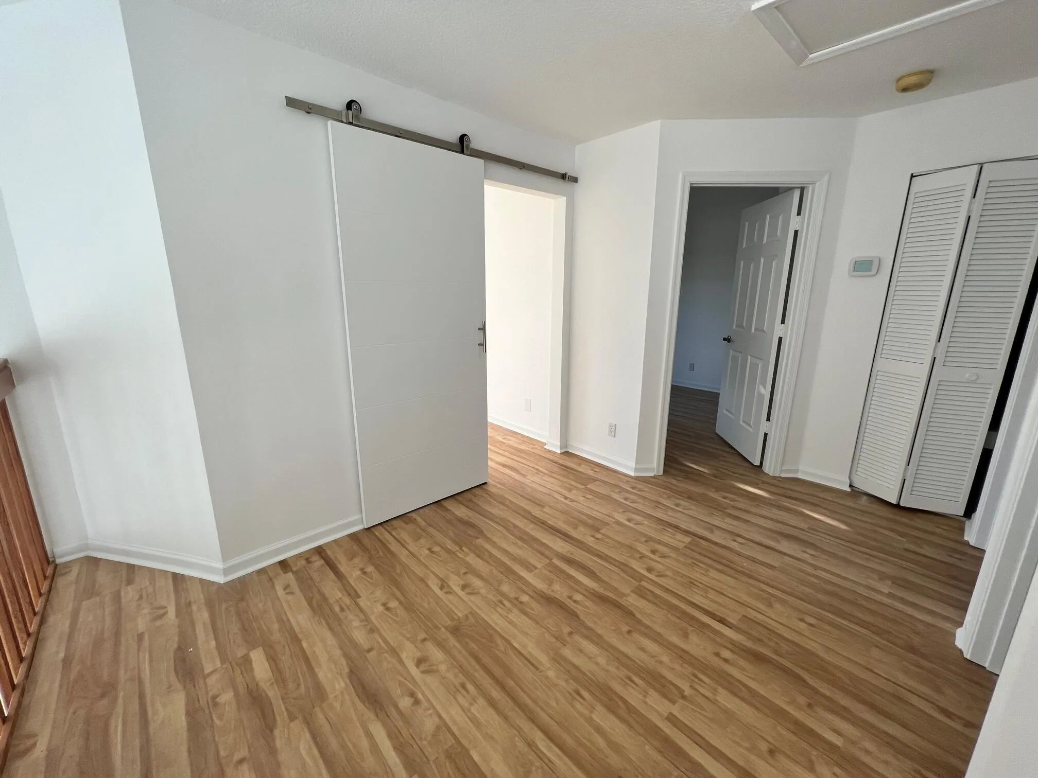 Open floor plan featuring wood-finish flooring, white baseboards, and a modern barn door on a stainless steel track