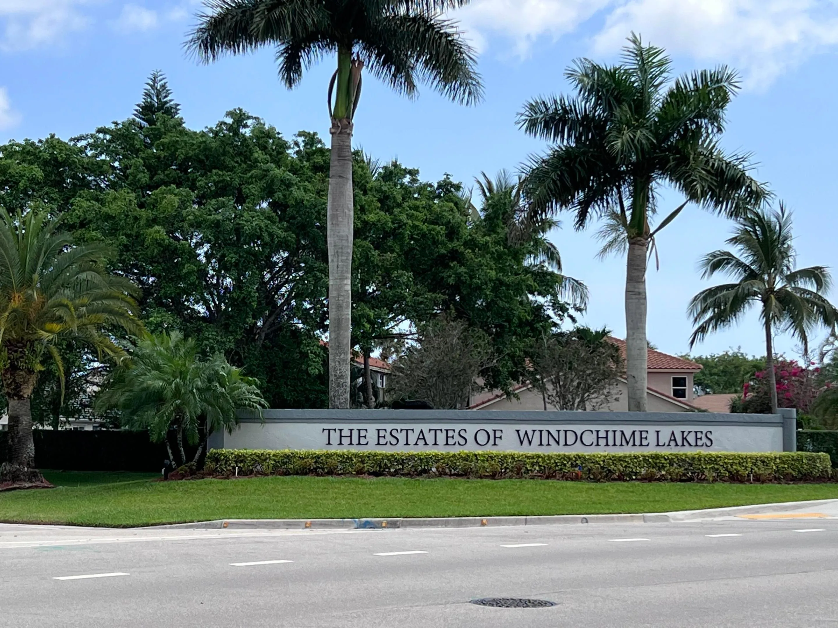 Community entrance sign for "The Estates of Windchime Lakes" featuring mature palm trees and manicured landscaping