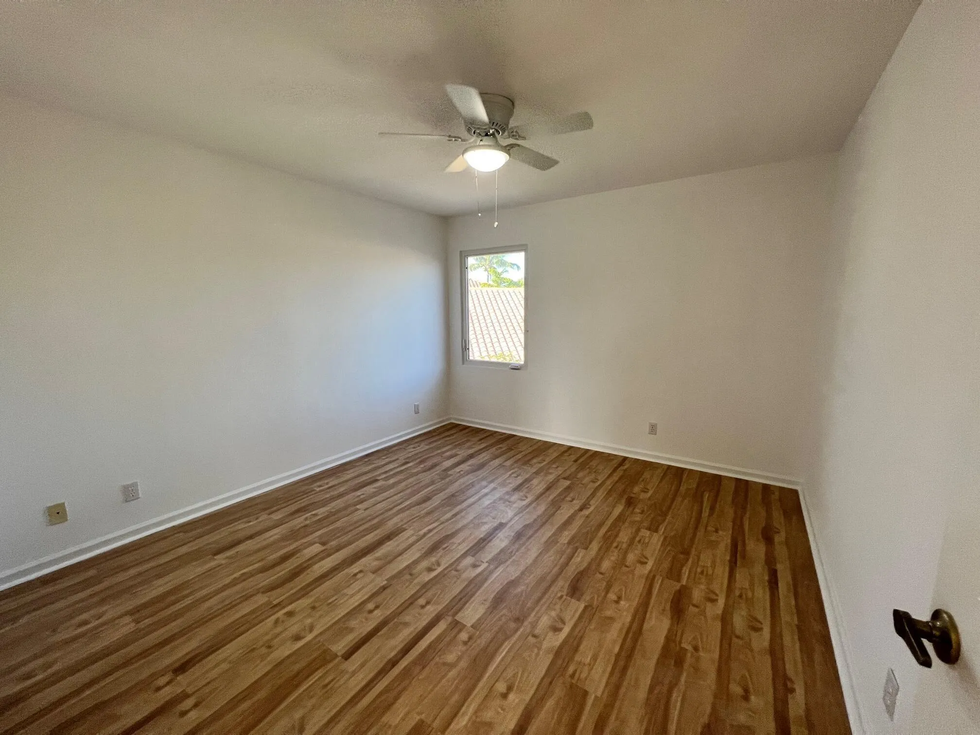 Spacious room featuring wood-finish flooring, white walls, and a ceiling fan with integrated lighting