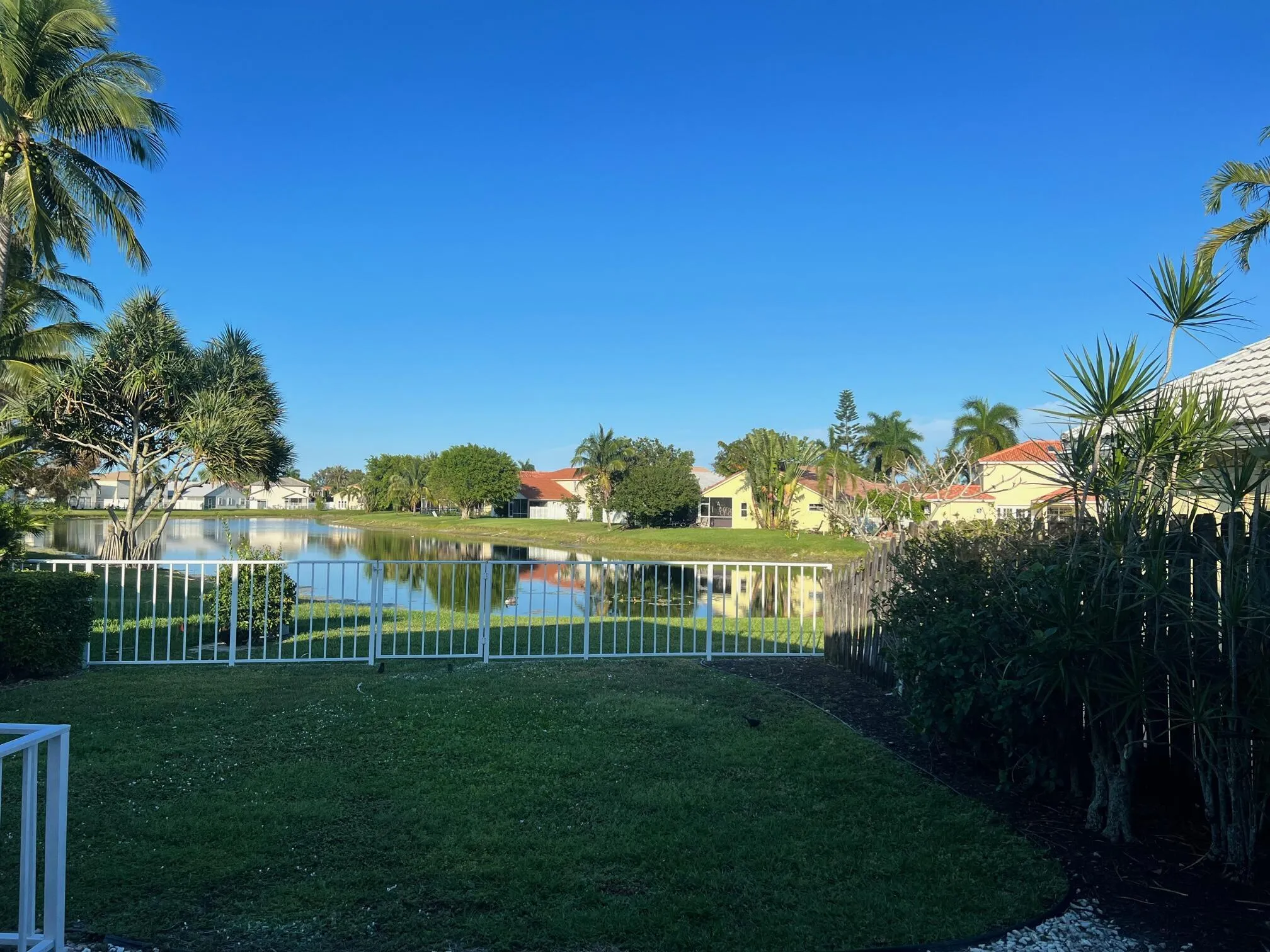 Manicured backyard with a white fence bordering a substantial lake
