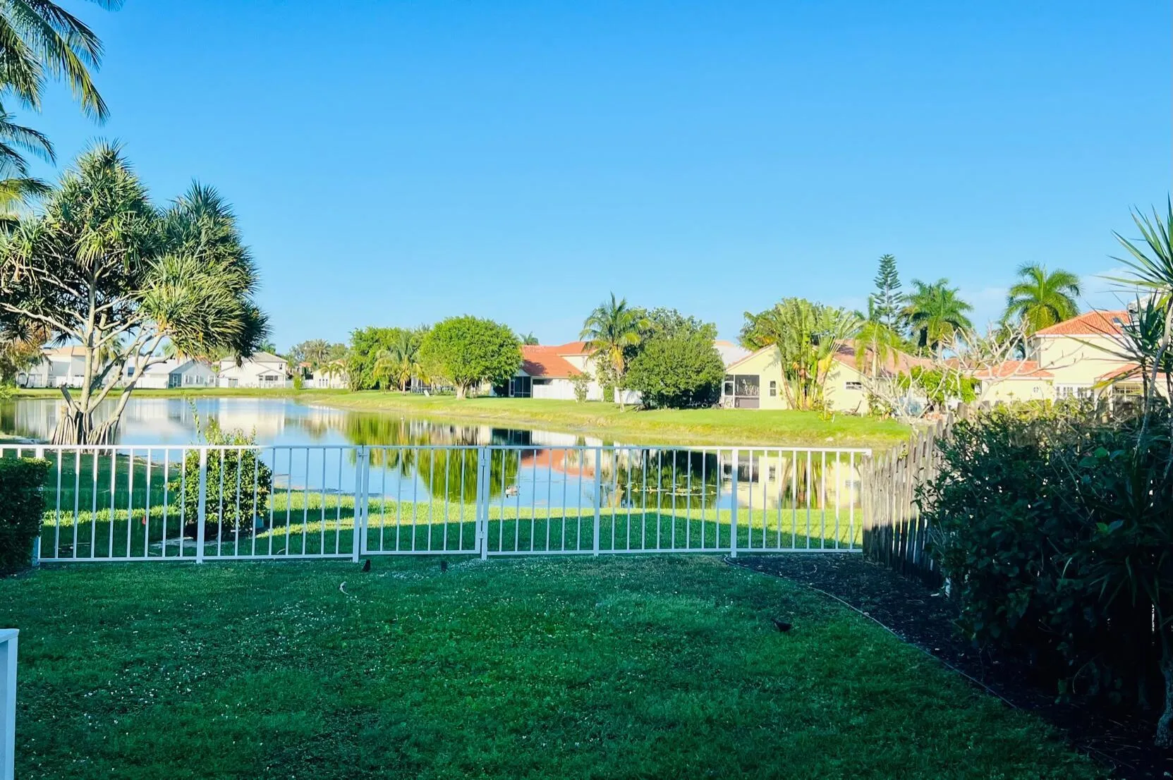 Expansive green lawn with a white metal fence bordering a serene body of water