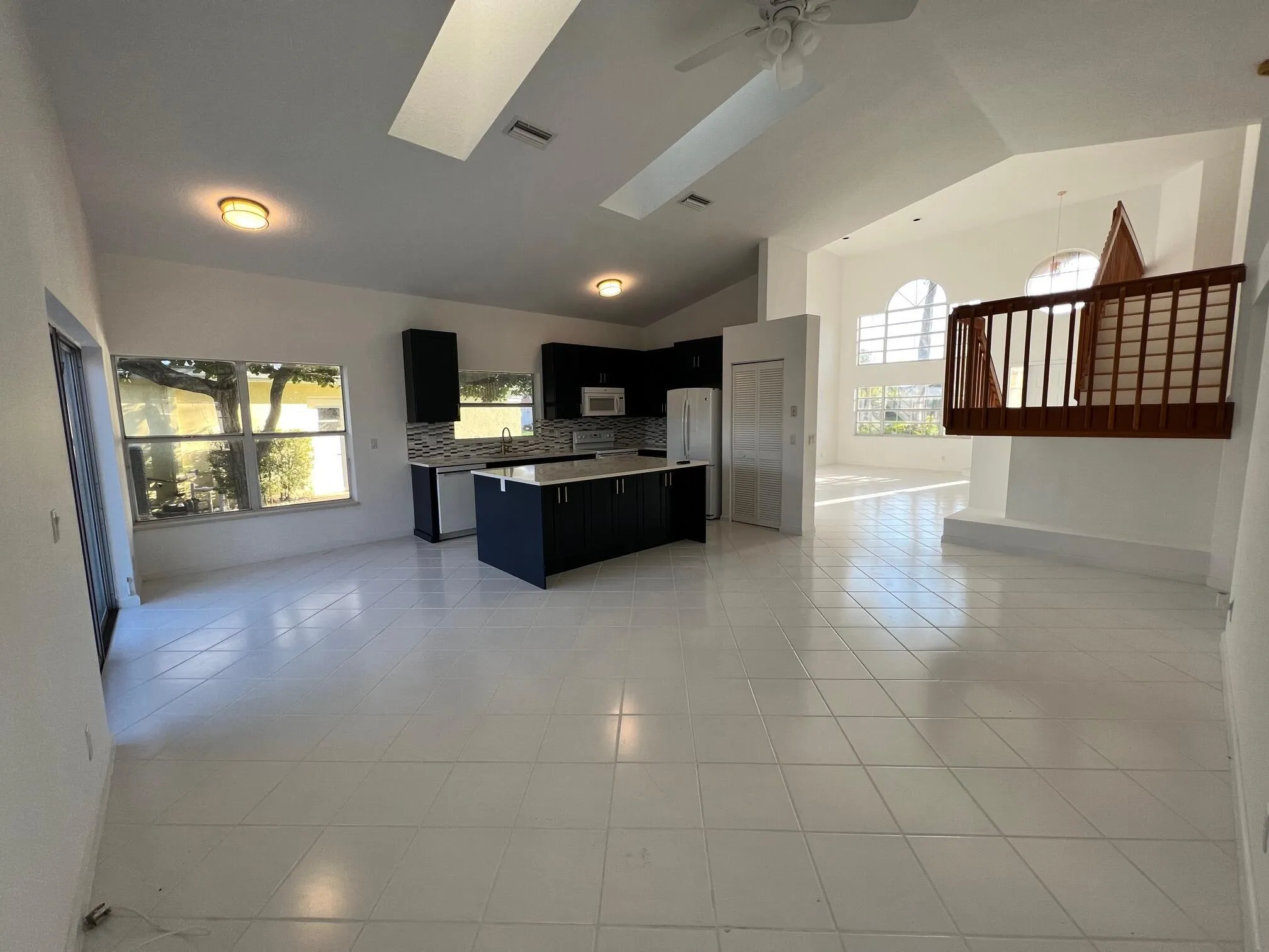 Open-concept living area with vaulted ceilings, skylights, and white tile flooring