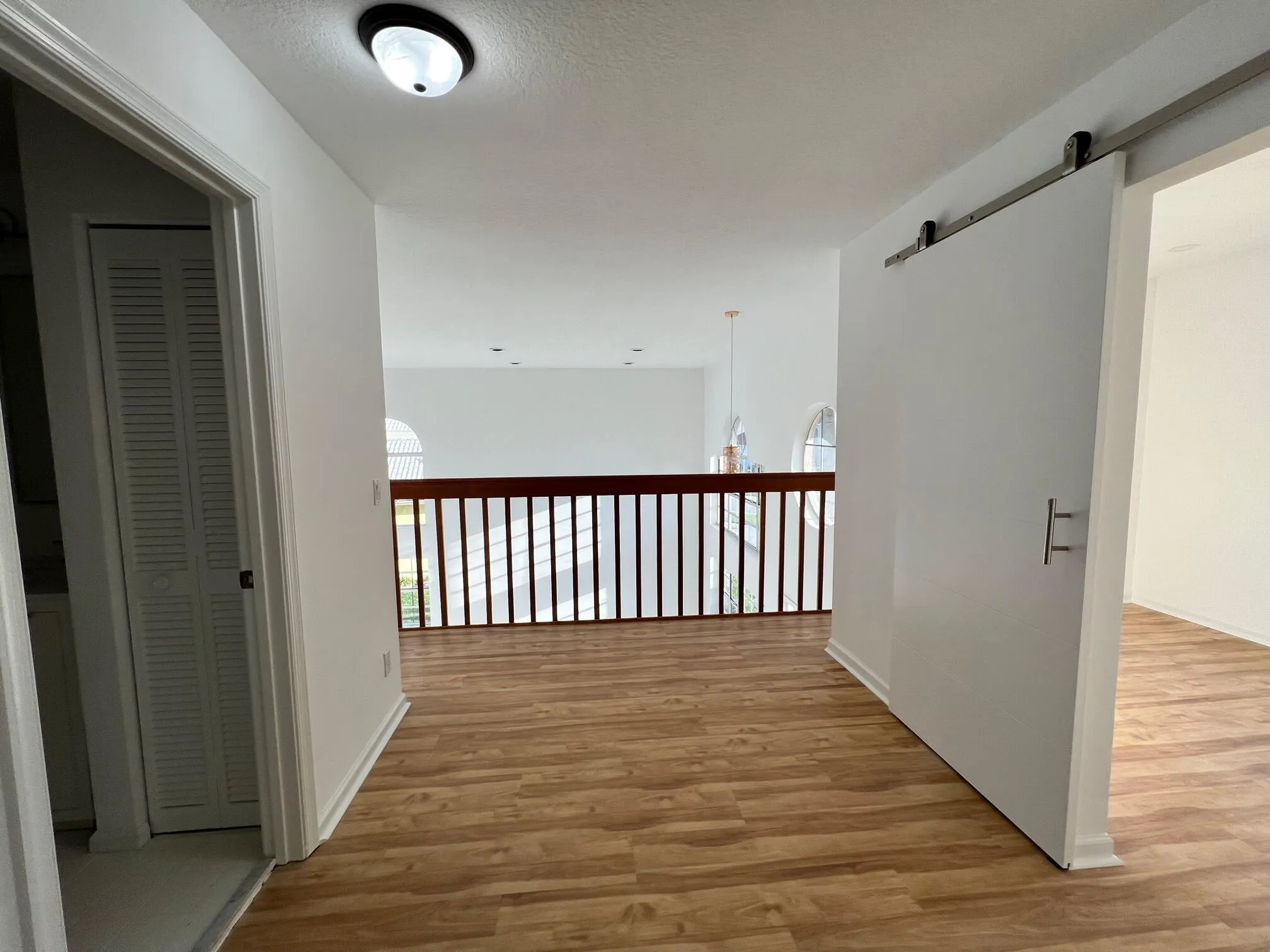 Upper-level landing featuring wood-finish flooring, a barn door entry, and a wood railing overlooking the lower level