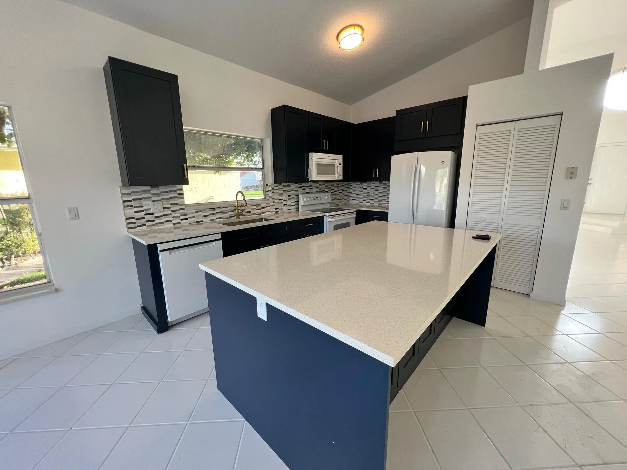 Kitchen featuring dark cabinetry, a spacious central island with a light-toned countertop, a tile backsplash, and white tile flooring