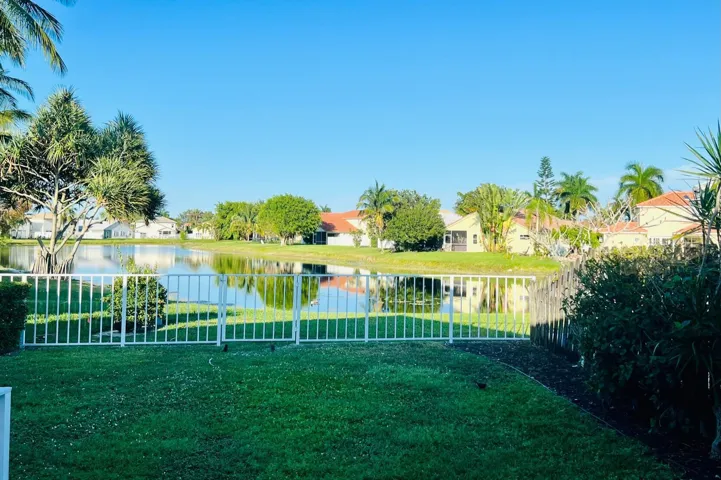 Expansive green lawn with a white metal fence bordering a serene body of water