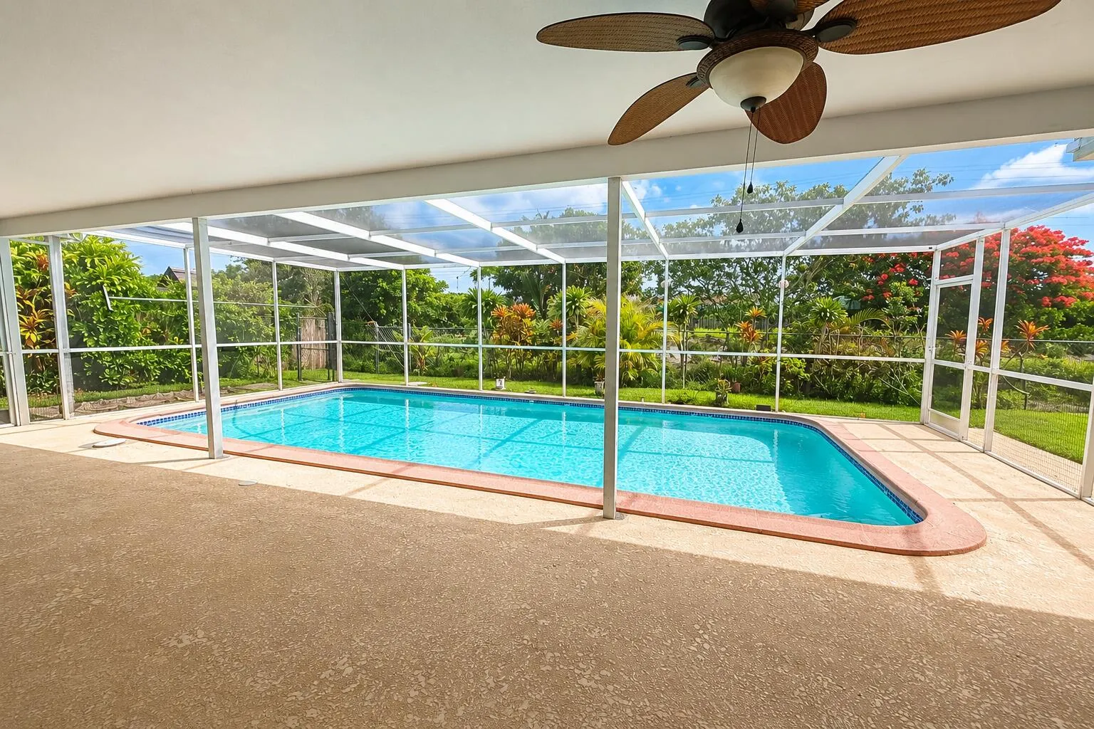 Screened-in patio with a textured concrete surface, offering an in-ground swimming pool with a tiled edge