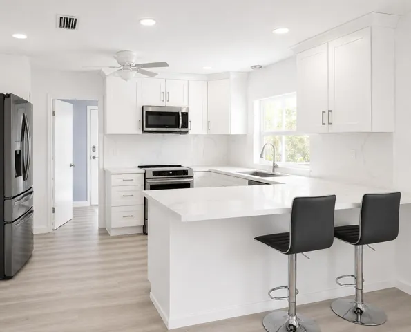 Bright kitchen featuring white shaker cabinetry, stainless steel appliances, a breakfast bar, recessed lighting, and wood-finish flooring