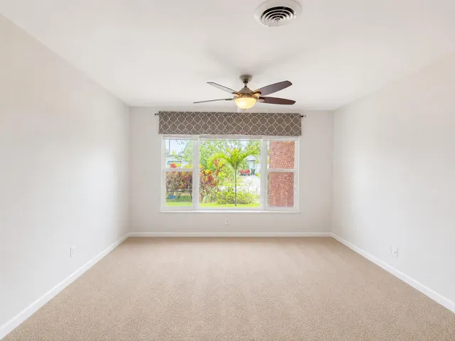 Carpeted interior space featuring a ceiling fan with wood-finish blades, two windows with blinds, white walls, and white baseboards