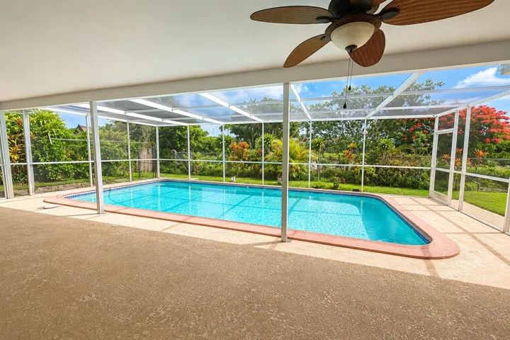 Screened-in patio with a textured concrete surface, offering an in-ground swimming pool with a tiled edge