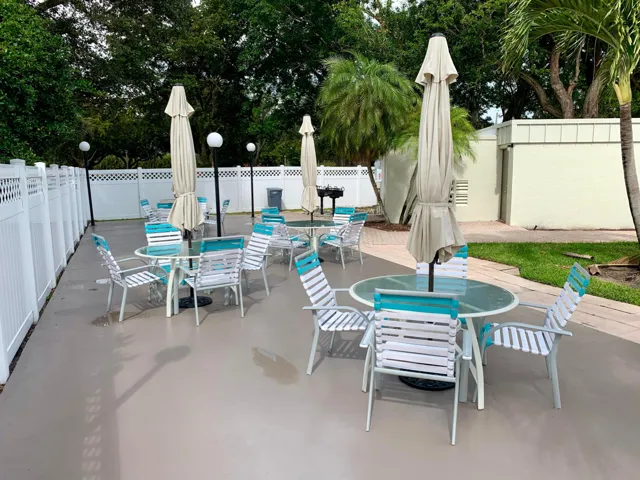 Spacious outdoor patio area featuring multiple seating arrangements, a built-in barbecue grill, perimeter fencing, and mature landscaping