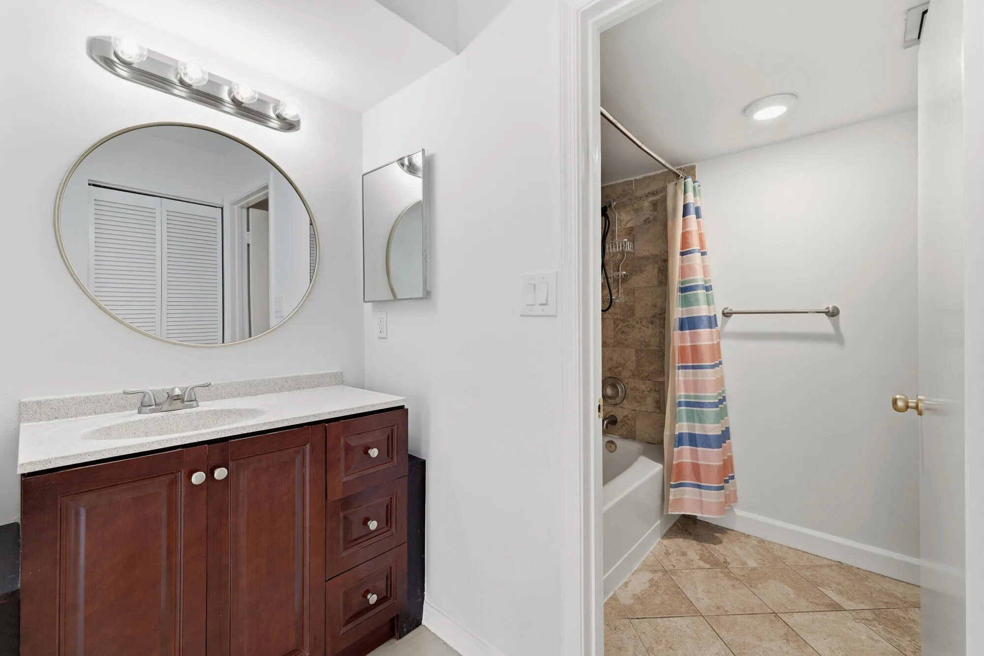 Bathroom featuring a dark wood-finish vanity with a light countertop, an oval mirror, and a four-bulb vanity light fixture
