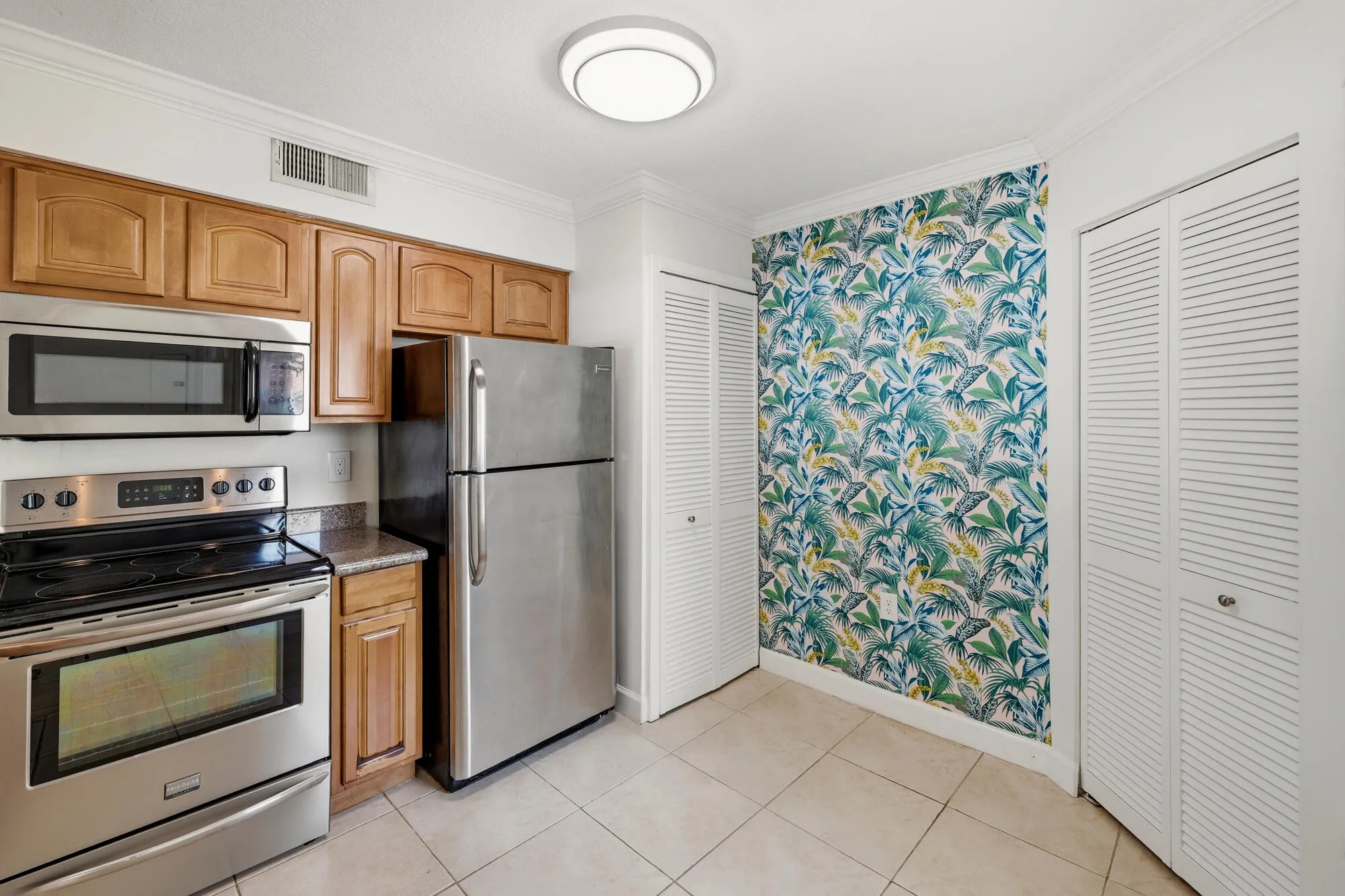Kitchen featuring stainless steel appliances, wood cabinetry, stone countertops, and tile flooring
