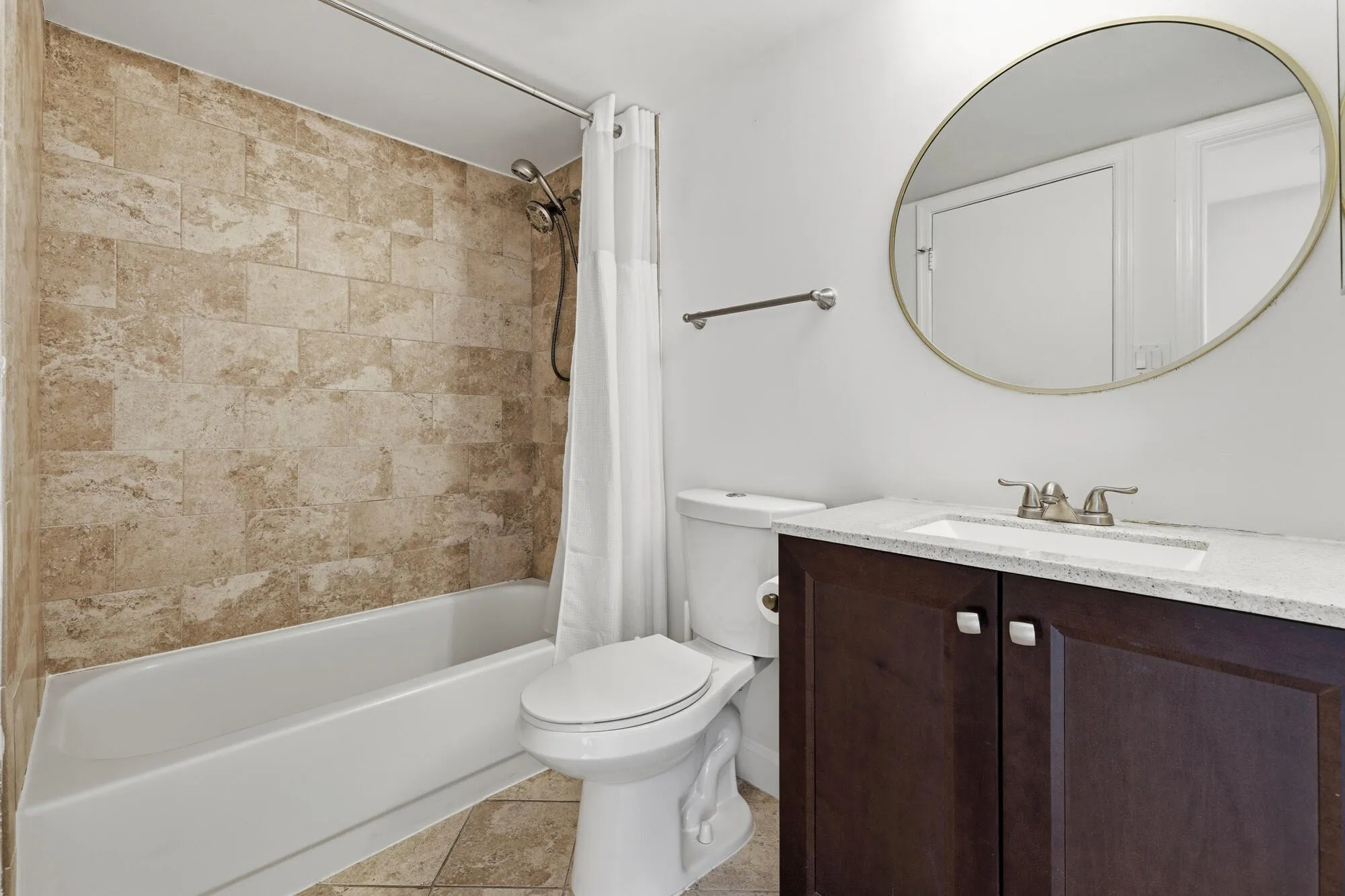 Bathroom featuring a tub/shower combination with tile surround, a dark wood-finish vanity with a light countertop, an undermount sink, and a circular wall mirror