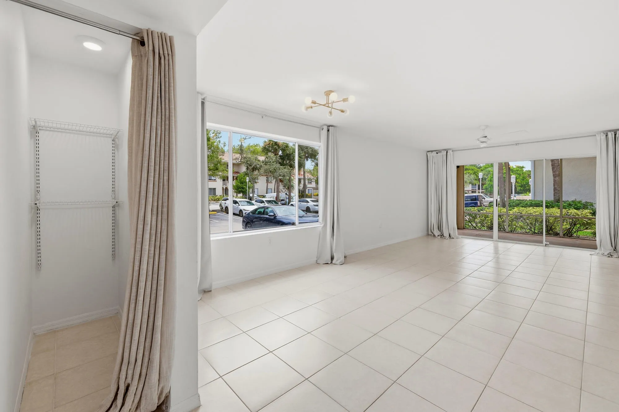 Spacious room featuring neutral tile flooring, a modern sputnik-style ceiling fixture, and a large window providing ample natural light