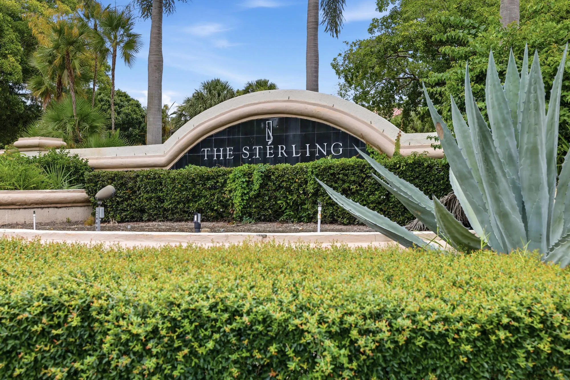 Curved stone entryway sign featuring "THE STERLING" lettering, dark stone backdrop, and integrated landscaping