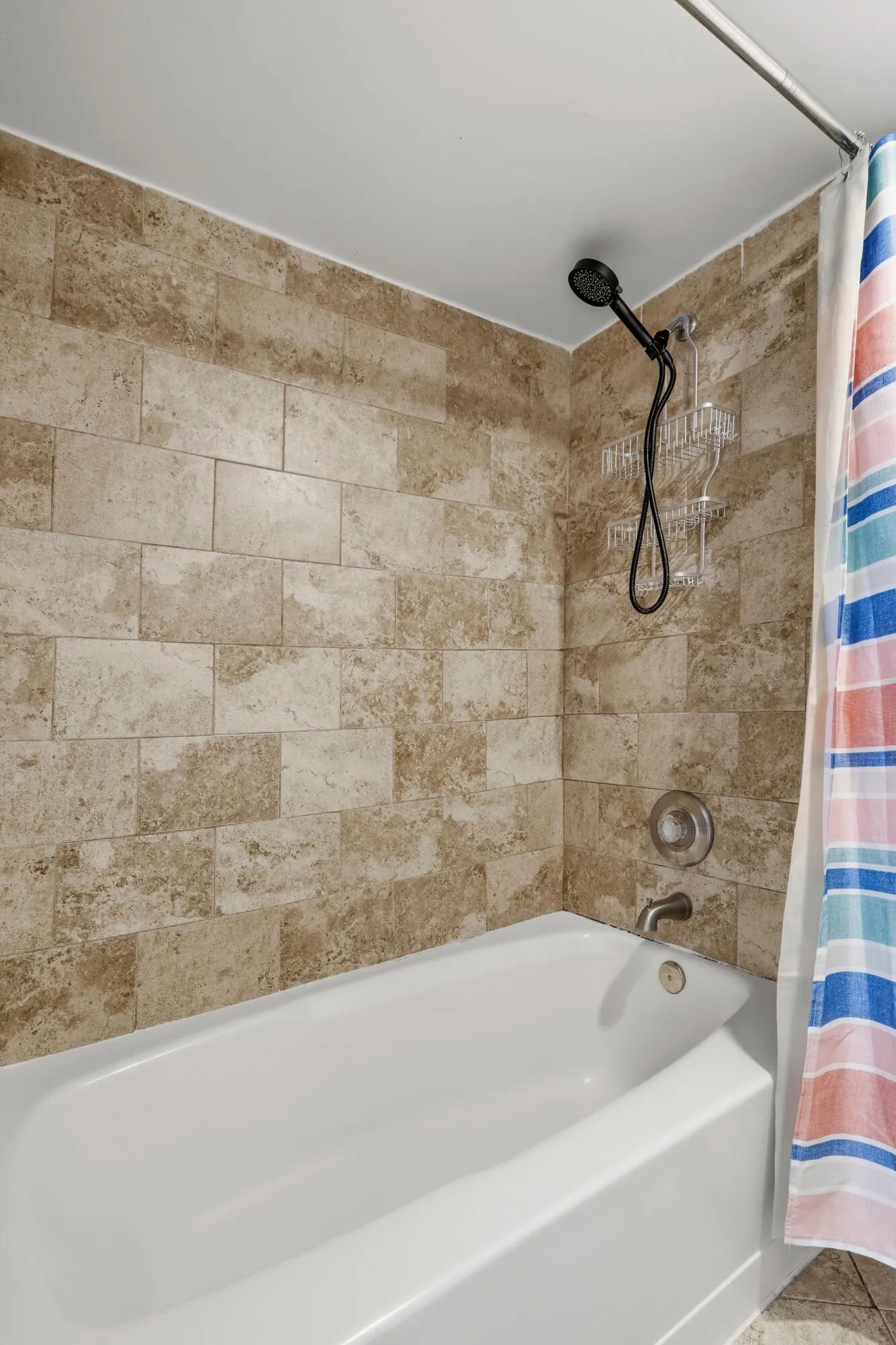 Bathtub and shower combination featuring neutral-toned tile surround, white tub, and a matte black shower head fixture