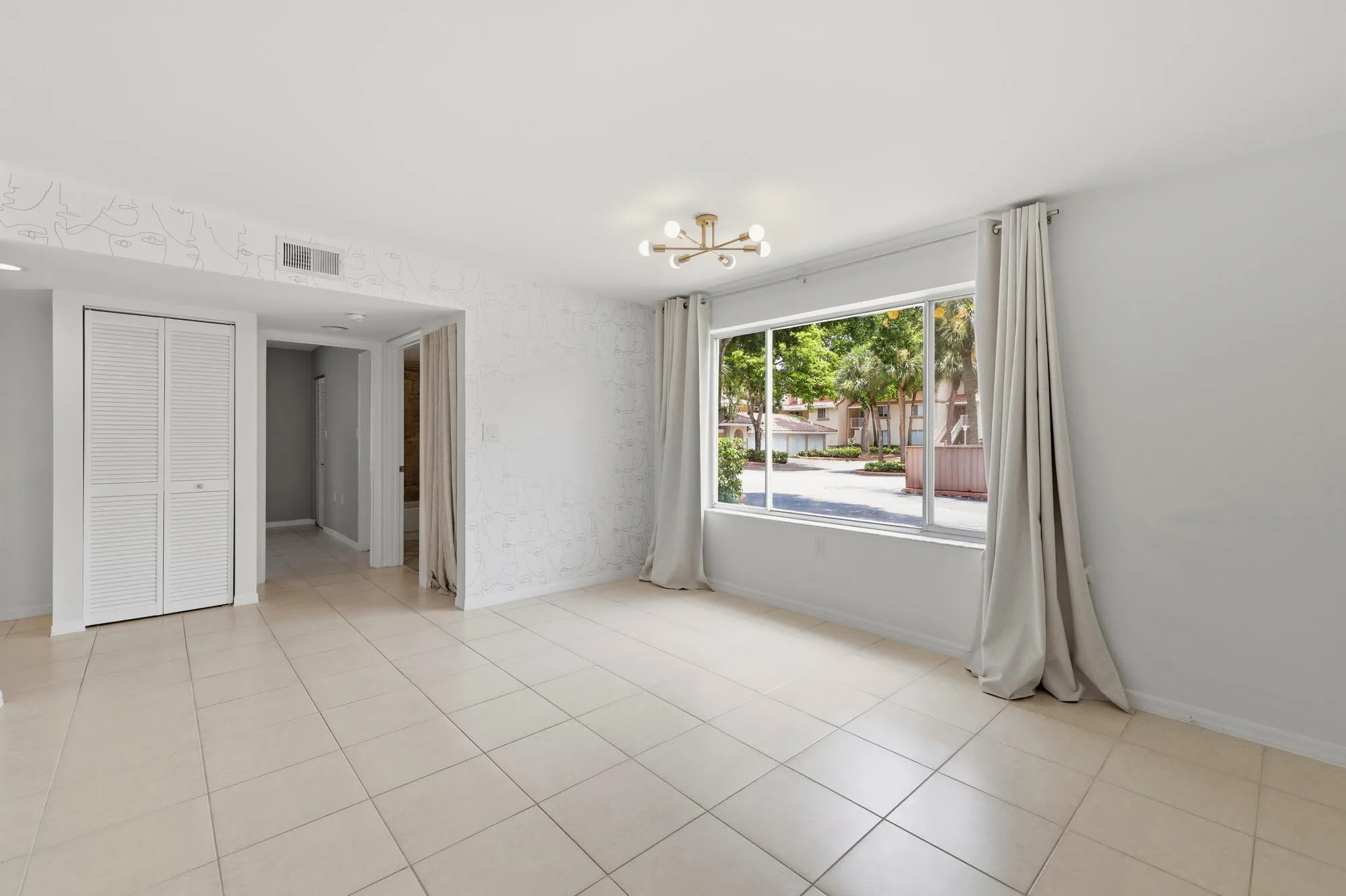 Bright living space featuring large format tile flooring, a modern sputnik light fixture, and a wide window with exterior landscaping