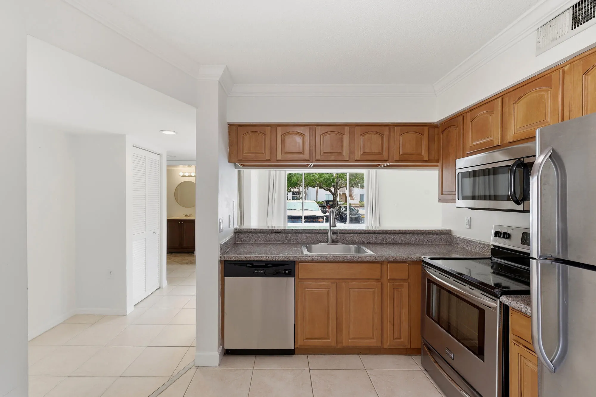 Kitchen featuring wood cabinetry, stainless steel appliances, a stone-finish countertop, and tile flooring