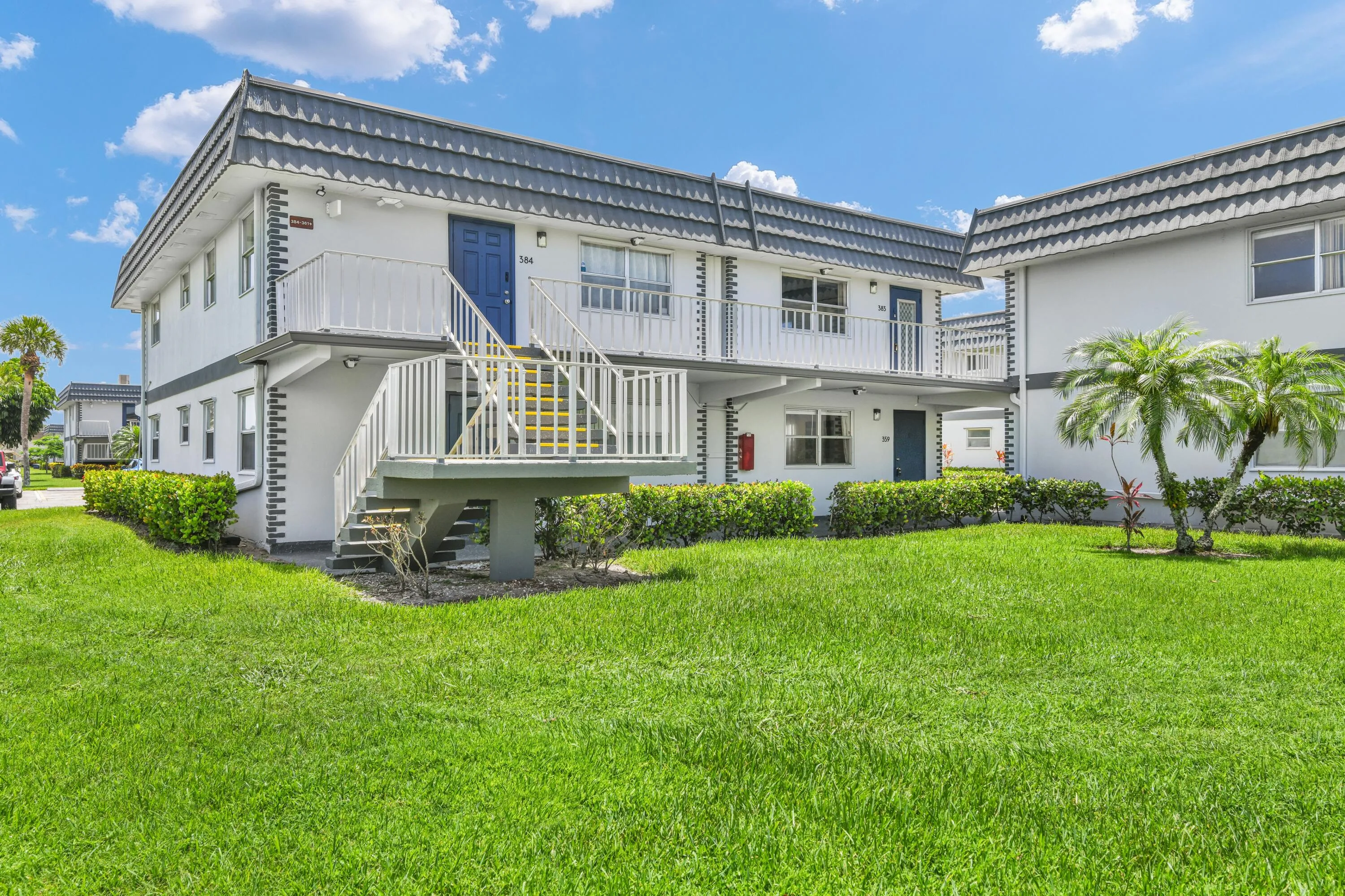 Two-story multi-unit building featuring white stucco exterior, grey metal roofing, and blue entry doors