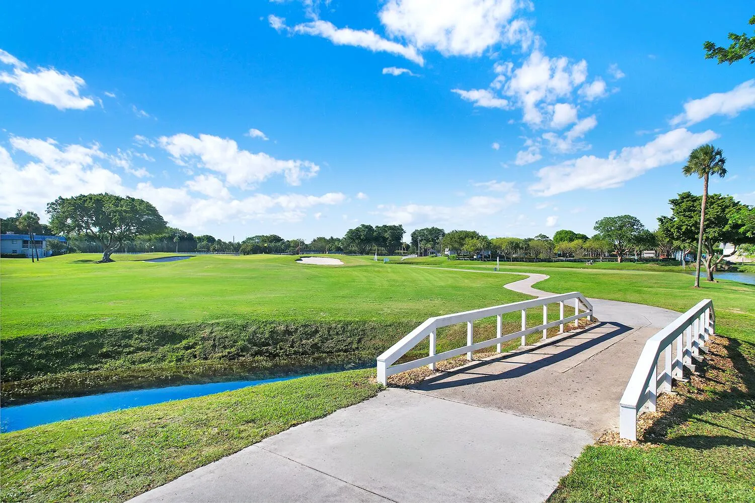 Golf course frontage featuring a cart path, white bridge, water feature, and mature trees