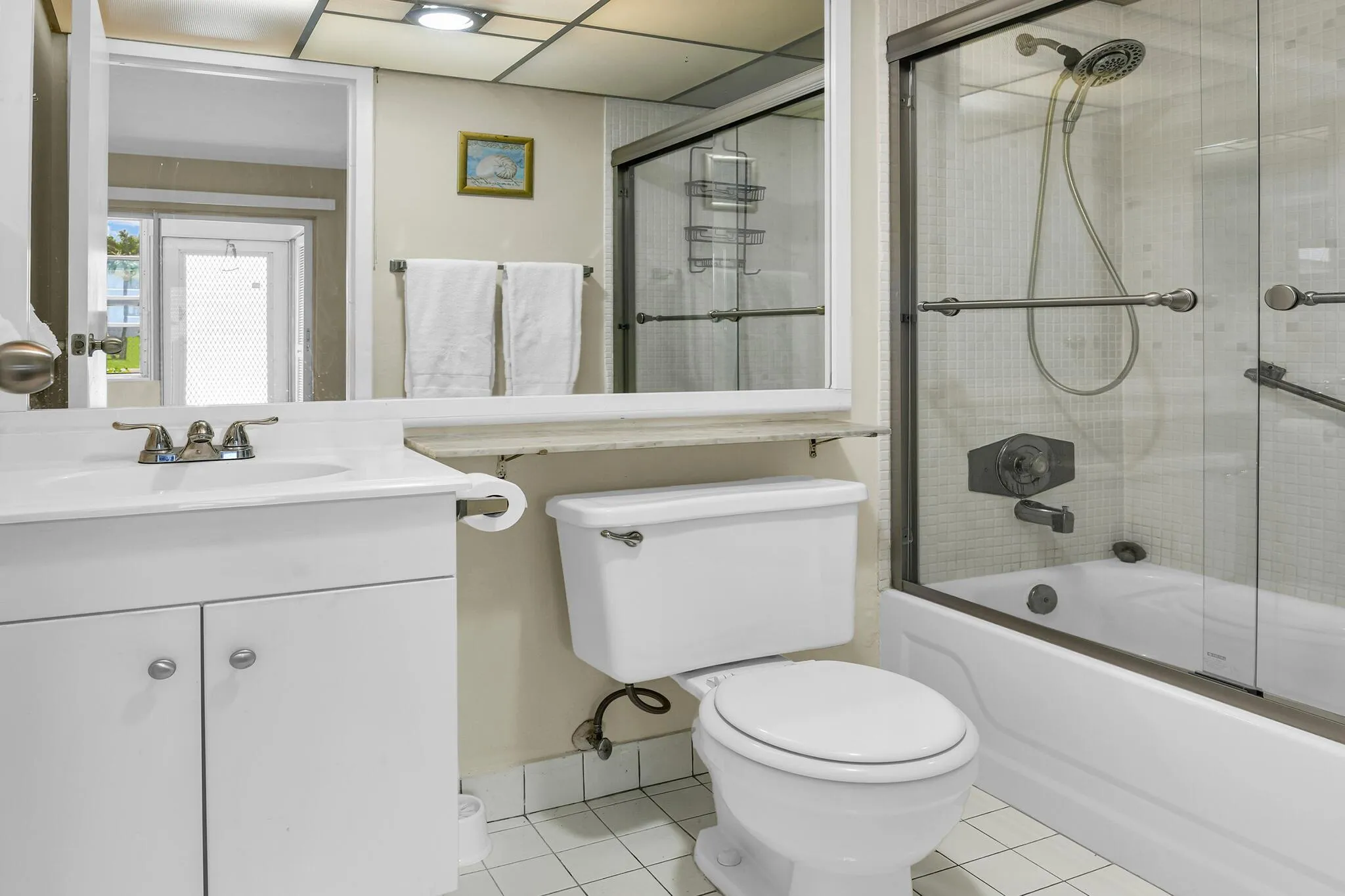 Bathroom featuring a glass-enclosed tub/shower combination, white vanity with cabinet storage, a toilet, and grid-patterned ceiling lighting