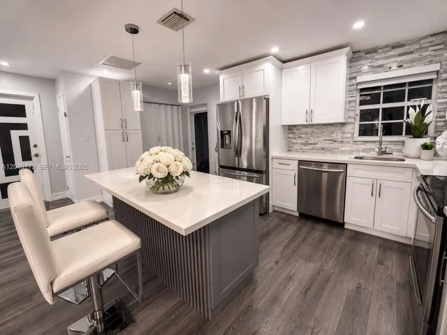 Beautifully renovated kitchen featuring white shaker cabinetry, quartz countertops, stainless steel appliances, a designer tile backsplash, and abundant storage.