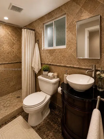 Private en-suite bathroom featuring marble flooring, floor-to-ceiling travertine stone, and a spacious walk-in shower with timeless natural finishes.