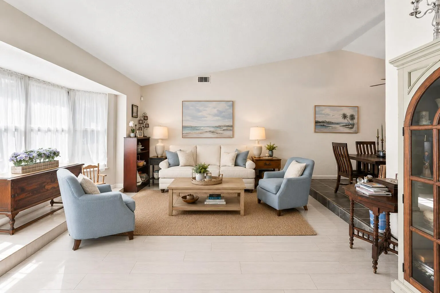 Vaulted ceilings accentuating a living area with light-toned wood-finish flooring and a bay window, with a dining area featuring dark tile flooring