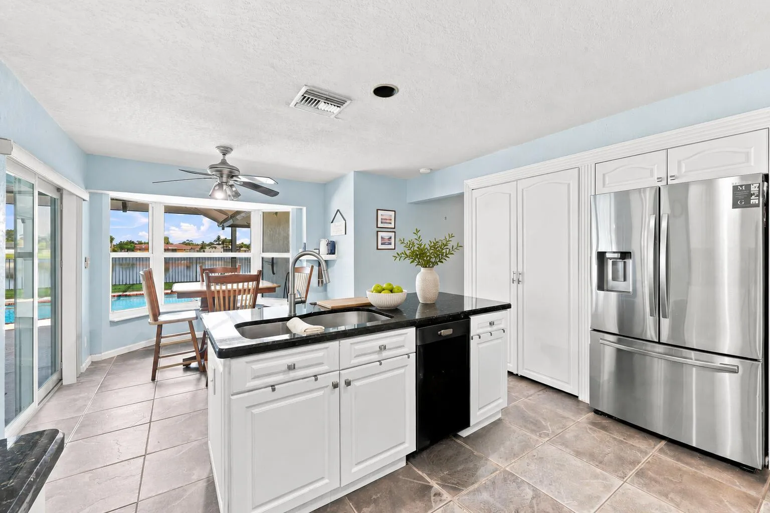 Kitchen featuring a central island with a sink, white cabinetry, stainless steel appliances, and tile flooring