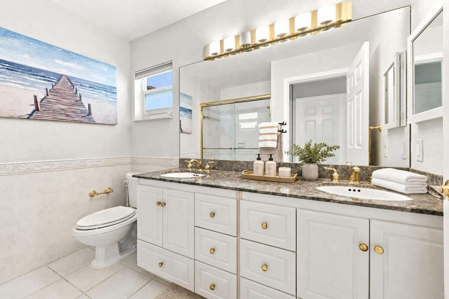 Dual vanity featuring white cabinetry with gold-tone hardware and a stone-finish countertop