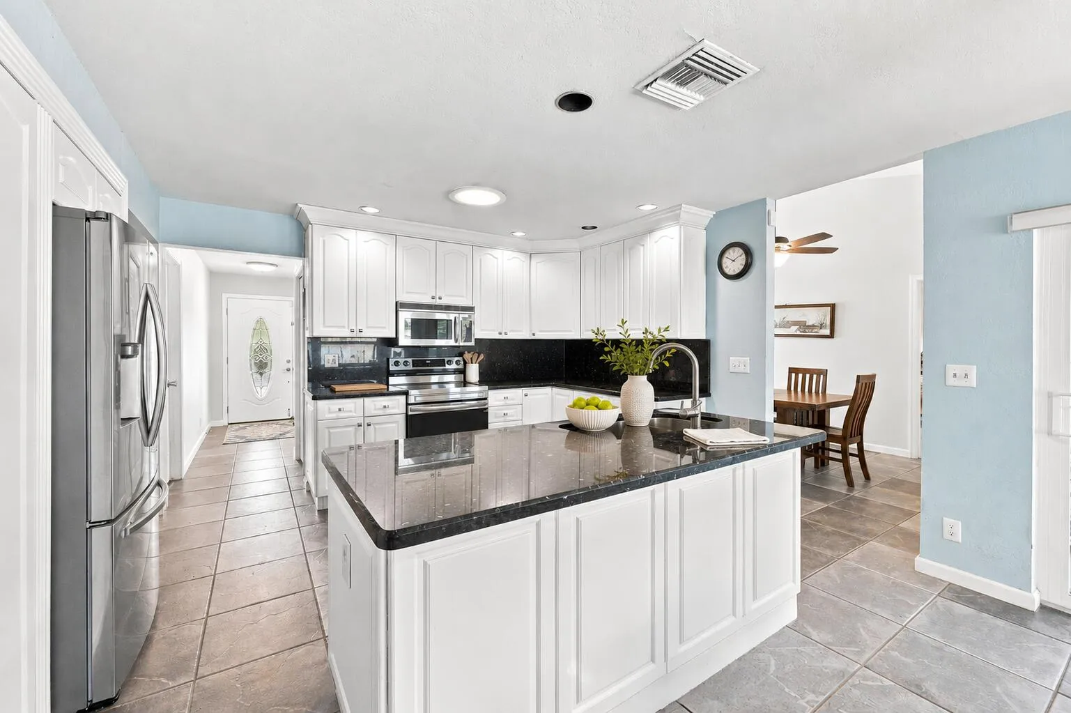Kitchen featuring white cabinetry, dark stone countertops, stainless steel appliances, and a central island with a built-in sink