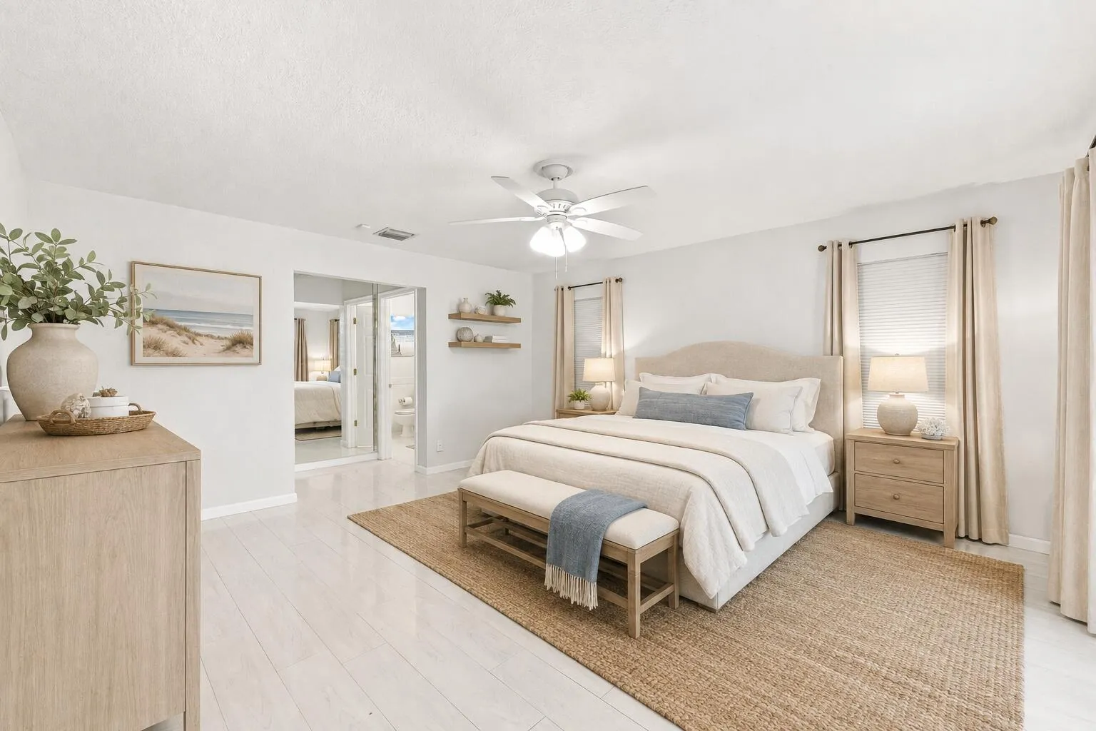 Spacious bedroom featuring light wood-finish flooring, a ceiling fan, dual windows with drapery, and a clear entryway into an adjacent room