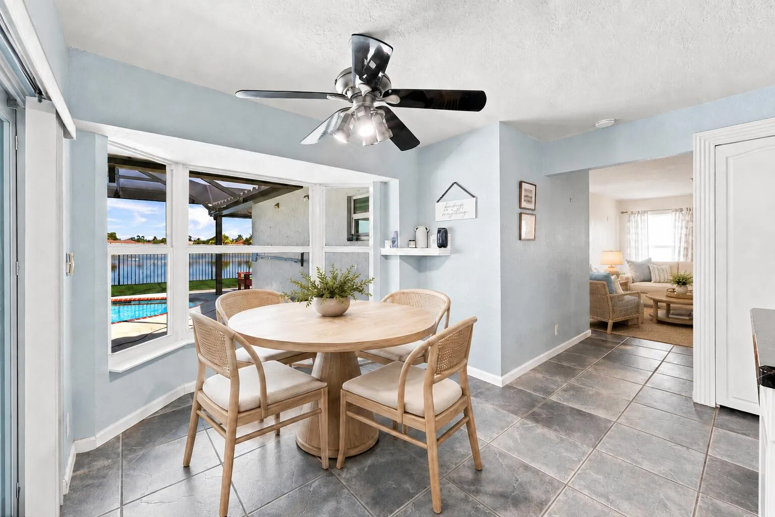 Dining area featuring large bay windows, water views, pool access, tiled flooring, and a ceiling fan with integrated lighting