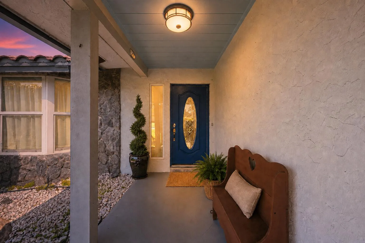Covered entryway featuring a blue front door with an oval stained-glass insert, recessed ceiling lighting, and a textured stucco exterior