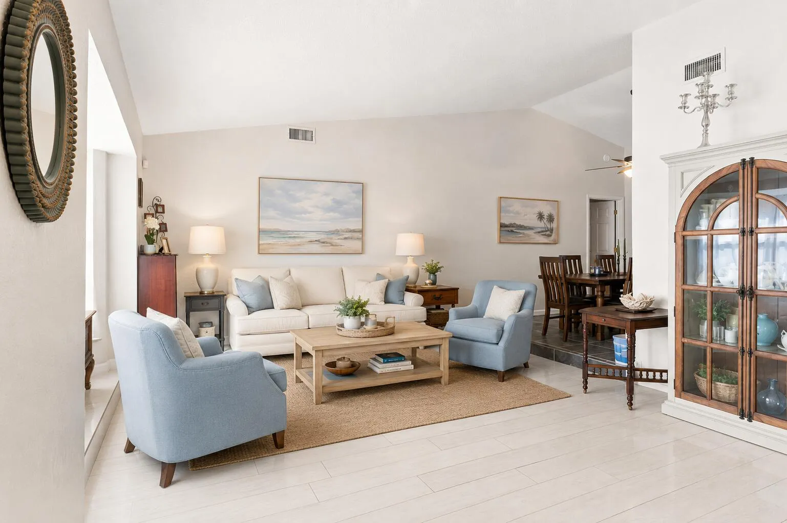 Vaulted ceilings highlight the bright living area, featuring light wood-finish flooring, a neutral color palette, and a dining area visible in the background