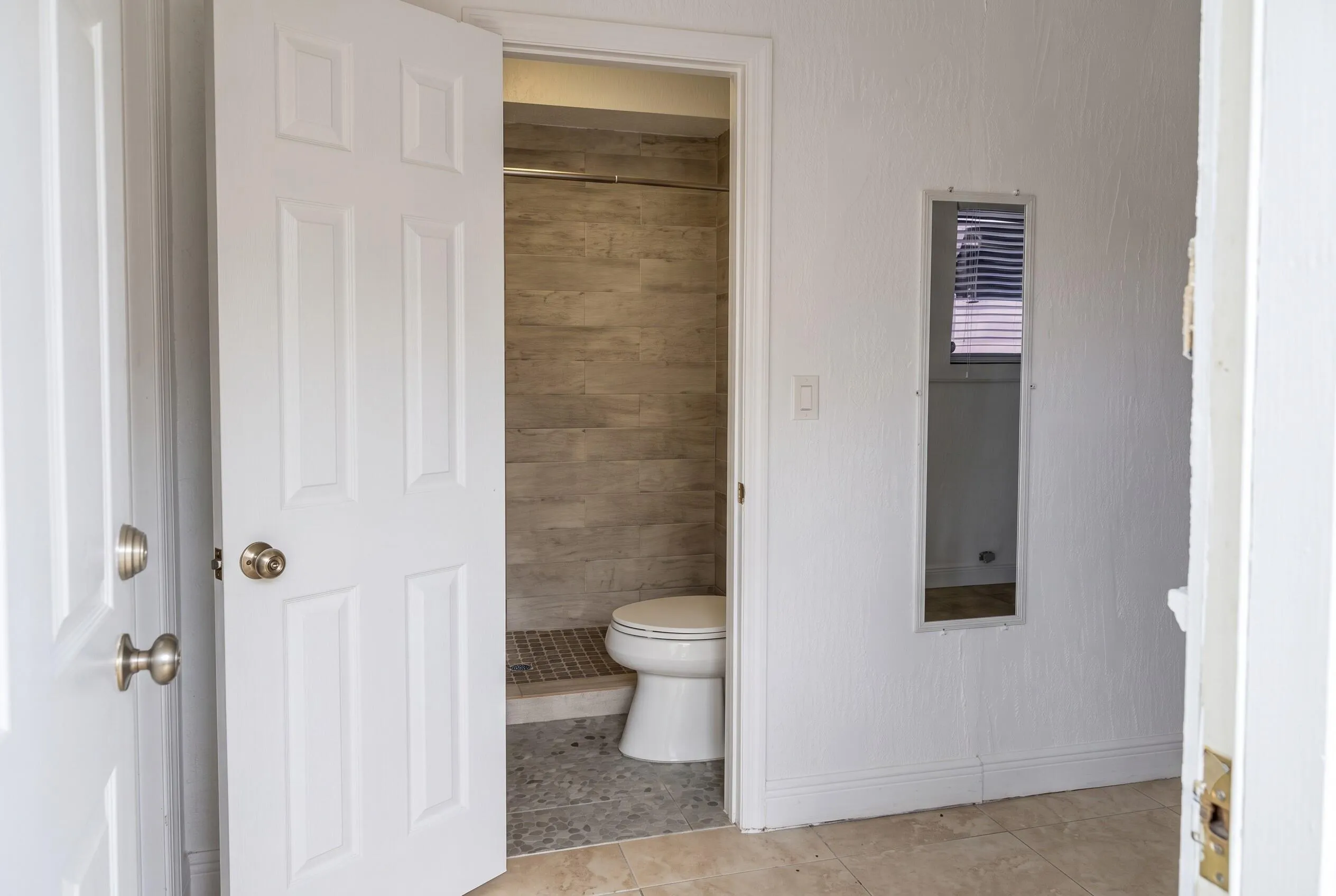 Bathroom featuring a tiled shower stall with a toilet, wood-finish wall tiling, and pebble-finish shower floor