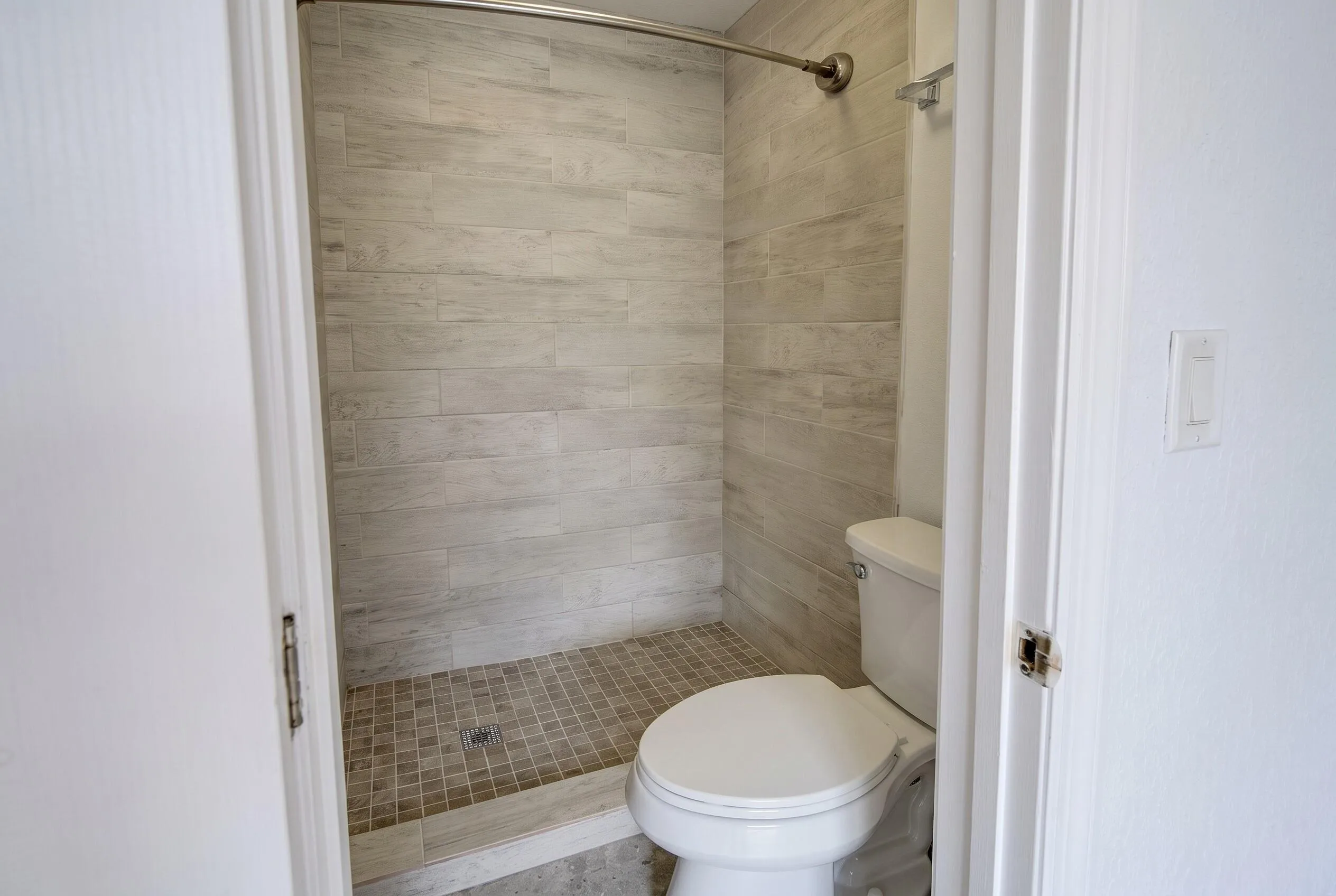 Bathroom featuring a walk-in shower with light-toned rectangular tile walls and a mosaic tile floor, alongside a white toilet