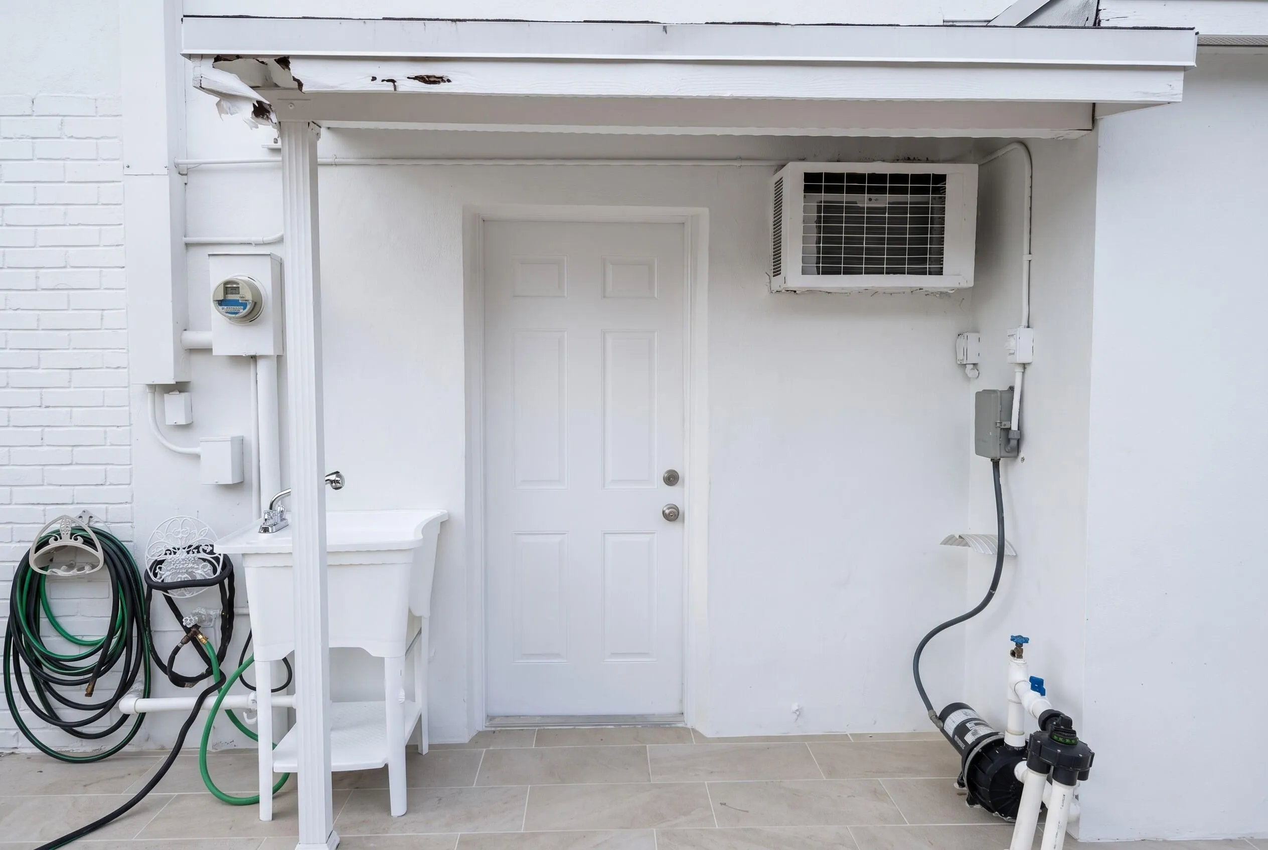 Exterior utility area featuring a white four-panel door, a window air conditioning unit, and a utility sink