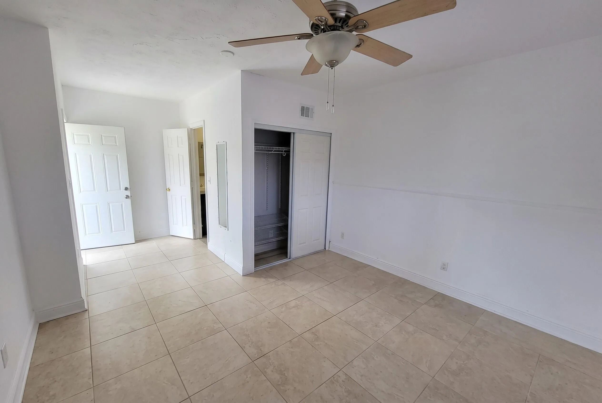 Neutral-toned tile flooring extends through this room featuring a ceiling fan with light, white baseboards, and a bi-fold door closet