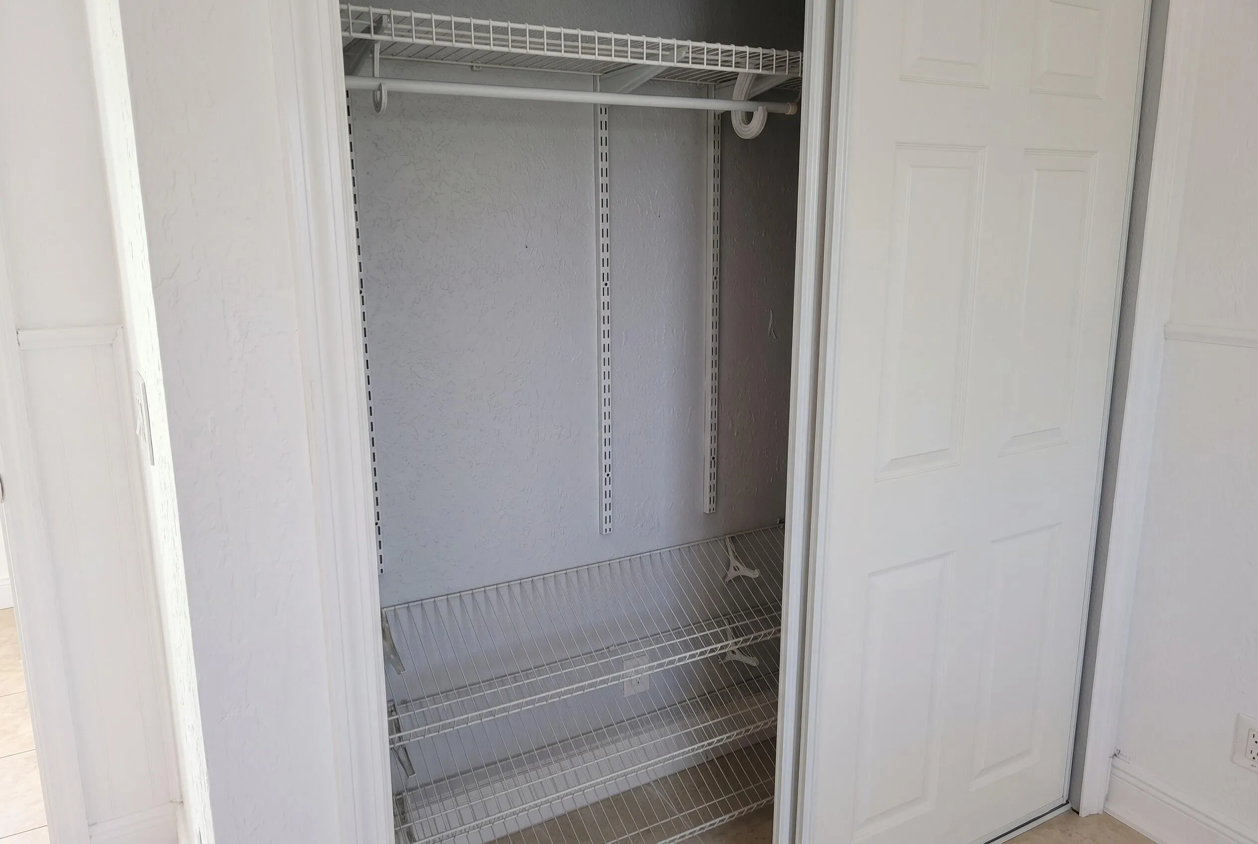 White wire shelving system with a hanging rod and multiple shelves, framed by white paneled bi-fold doors