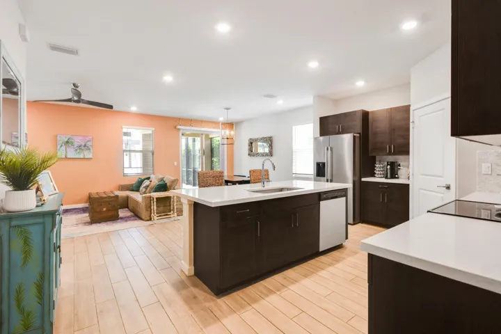 Open-concept kitchen featuring an island with a sink, stainless steel appliances, dark wood-finish cabinetry, and light wood-plank tile flooring