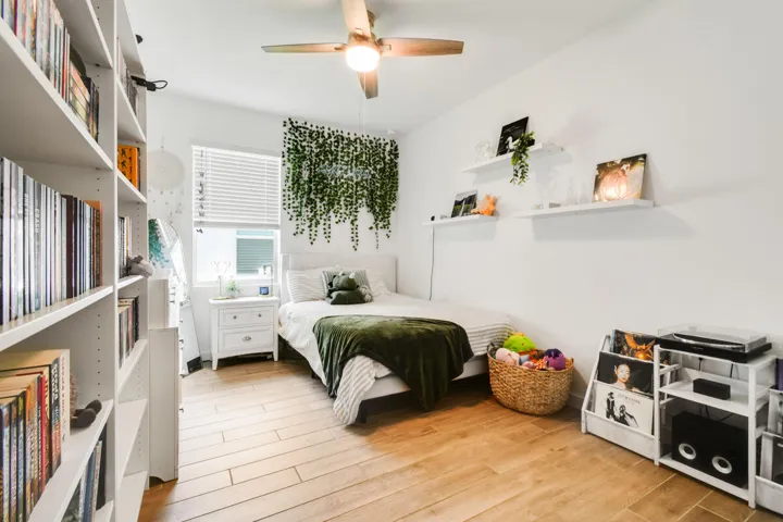 Spacious bedroom featuring wood-plank tile flooring, white walls, and a ceiling fan with integrated lighting