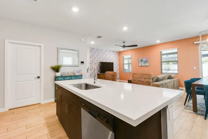 Kitchen island with a white quartz countertop and integrated stainless steel sink, dark wood-finish cabinetry, and built-in dishwasher